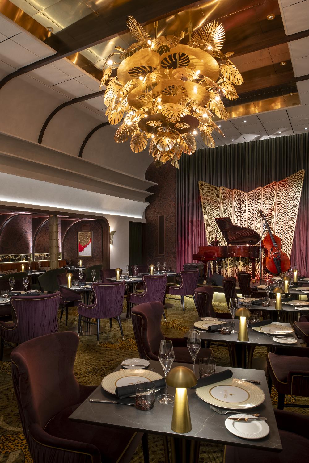 Supper club dining room with gold palm chandelier, velvet chairs and a live jazz stage
