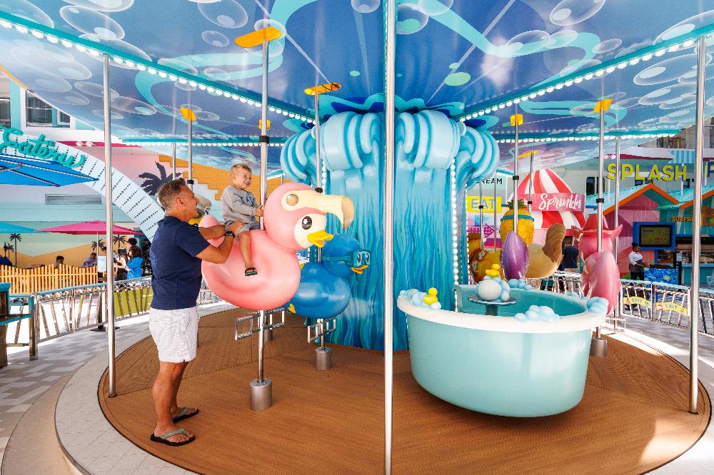 Father lifting his son onto a flamingo seat on the Surfside carousel