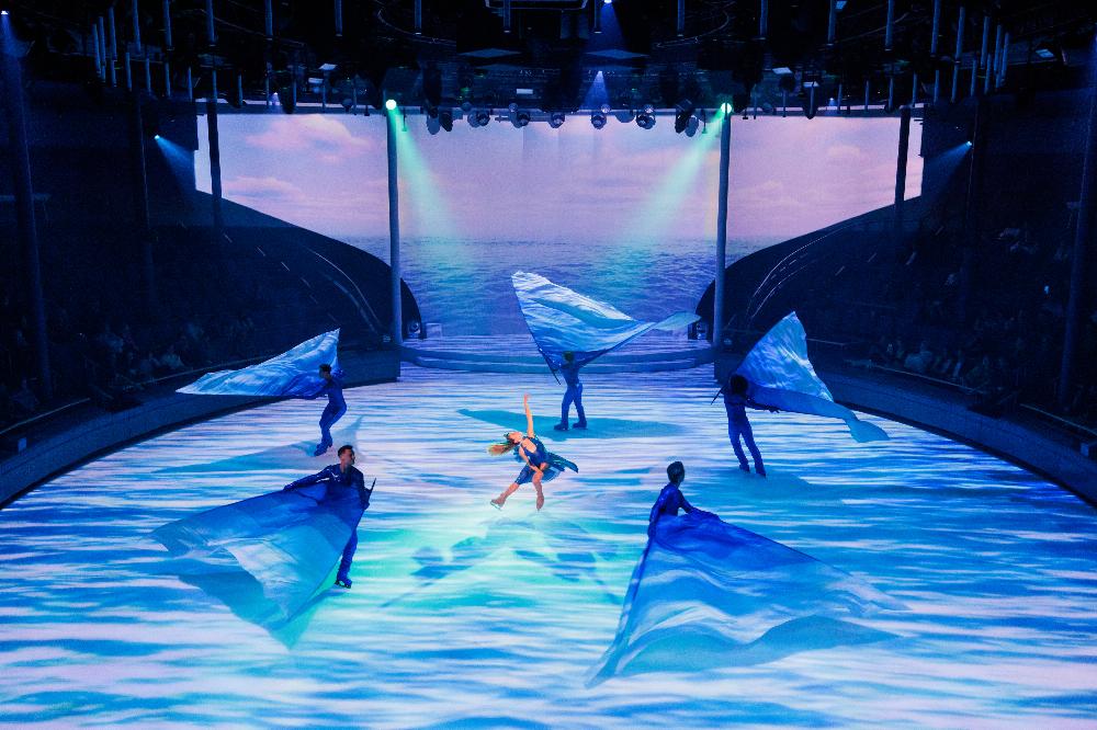 Ice skaters with flowing blue silks in an ocean-themed performance