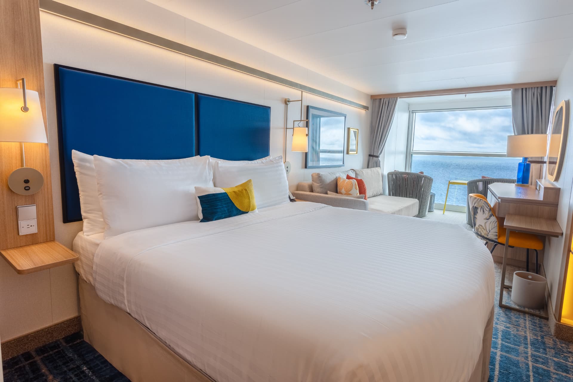 Family Infinite Ocean View Balcony stateroom with king bed, sofa and floor-to-ceiling ocean windows