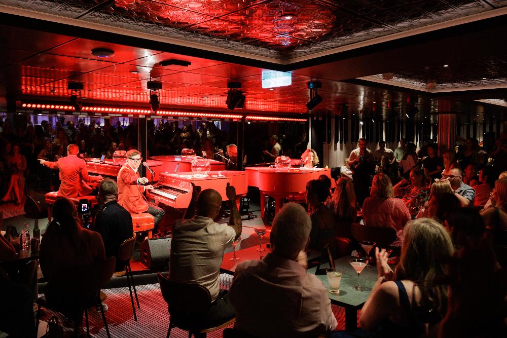 Guests watching performers at the red-lit dueling pianos bar