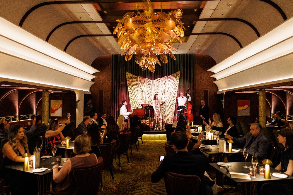Guests dining while a singer and jazz trio perform in an art-deco supper club