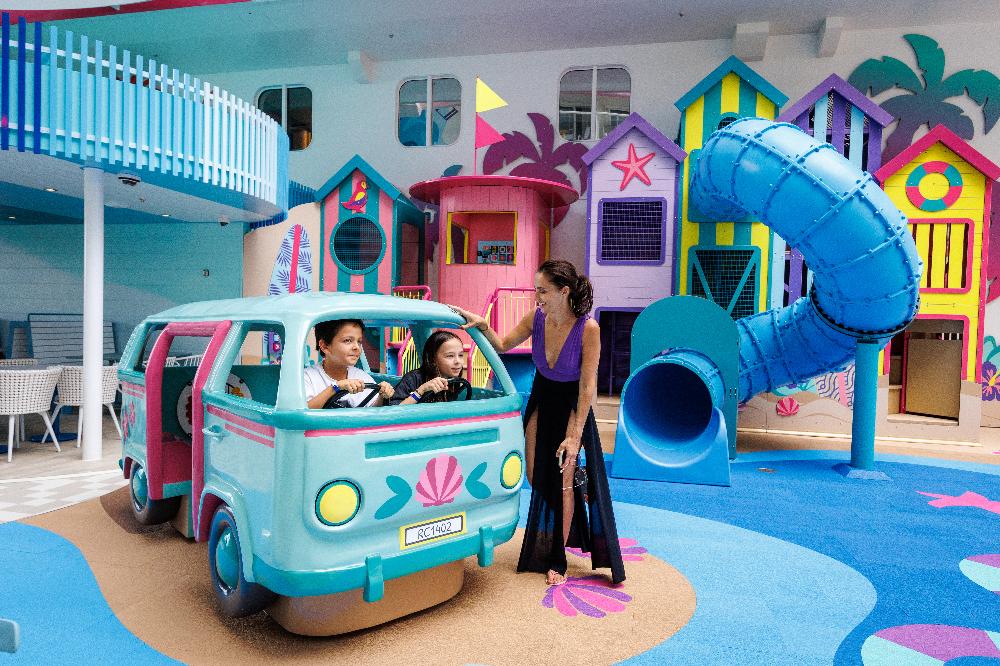 Mother and children playing in a beach-hut themed indoor playscape with tube slide